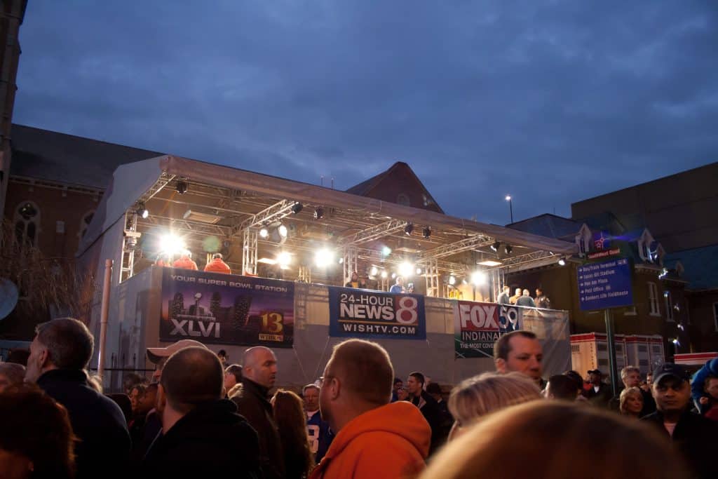front of house tech area in the middle of a crowd int he evening. FOH is covered in white soft good with sponsorship banners all around it.