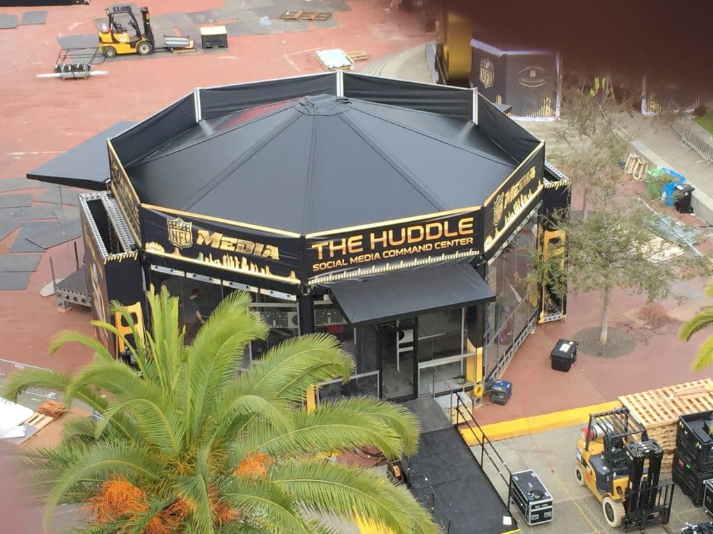Black soft good with gold NFL NETWORK logos and lettering surround a hexagonal structure at a large event. View is looking down on the top 3/4 view of this structure
