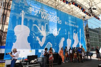Printed backdrop behind musicians on a stage. Backdrop is blue and white with the words "Boston Globe. WGBH, Summer Arts Weekend, presented by citizens bank"
