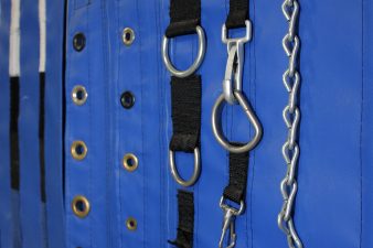 Cropped image: Various D-rings, grommets, and chains displayed on a blue vinyl wall. Accessories for attaching roof skins and side walls to stages and live event structures.